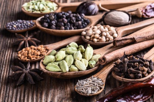 Different types of whole Indian spices in wooden spoons on rustic background close-up.  Black pepper, fenugreek, anise, cinnamon, cardamom, coriander, mustard, nutmeg, clove, cumin. Healthy food.